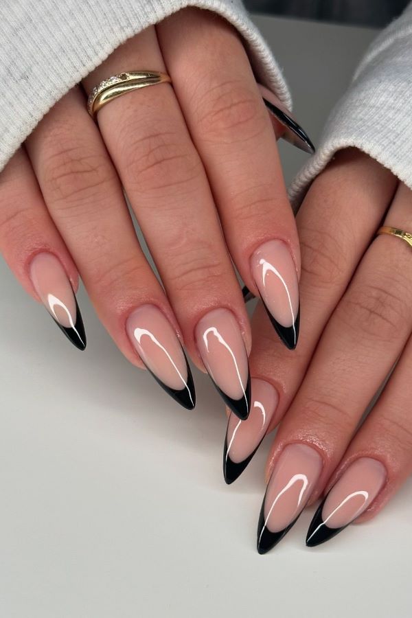 Hände mit schwarzen Stiletto-Nägeln mit einer schwarzen French Manicure.