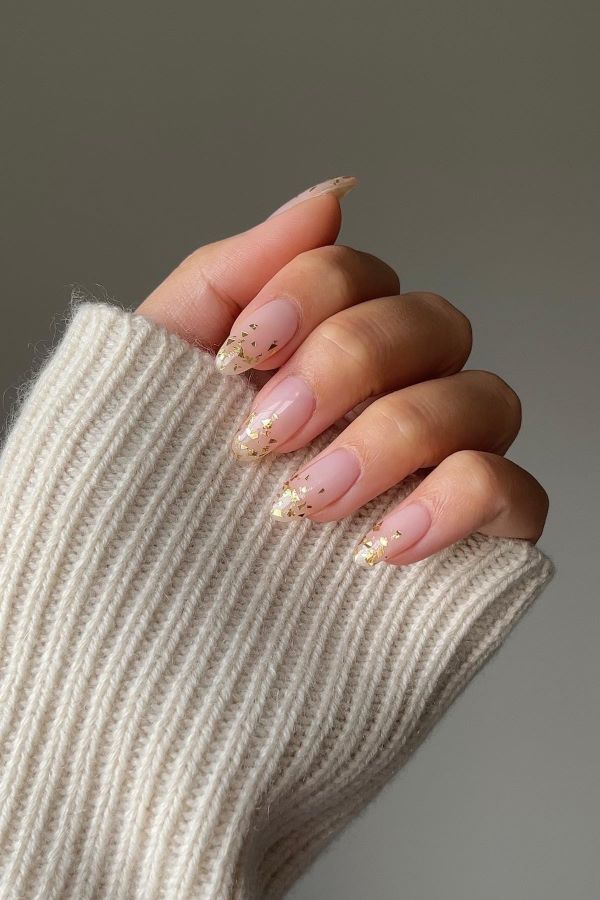 Hand mit roséfarbenem Nageldesign und Goldflocken an den Spitzen, ideal für einen eleganten und festlichen Look
