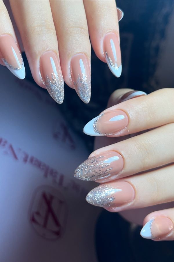 Mandelförmigen Nägeln in Nude mit weißen Spitzen und silbernem Glitzergradient, glänzend und elegant.