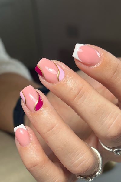 Kurz und schick: Entdecke dieses verspielte Nailart-Design mit rosa und goldenen Wellen auf einer französischen Basis.