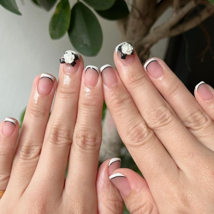 Klassische French Nails mit feiner schwarzer Linie und zarten 3D-Rosen auf den Daumennägeln.