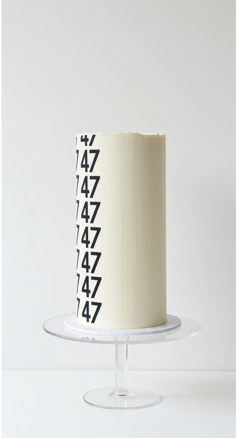 Hohe weiße Torte mit vertikal wiederholter schwarzer Zahl 47.